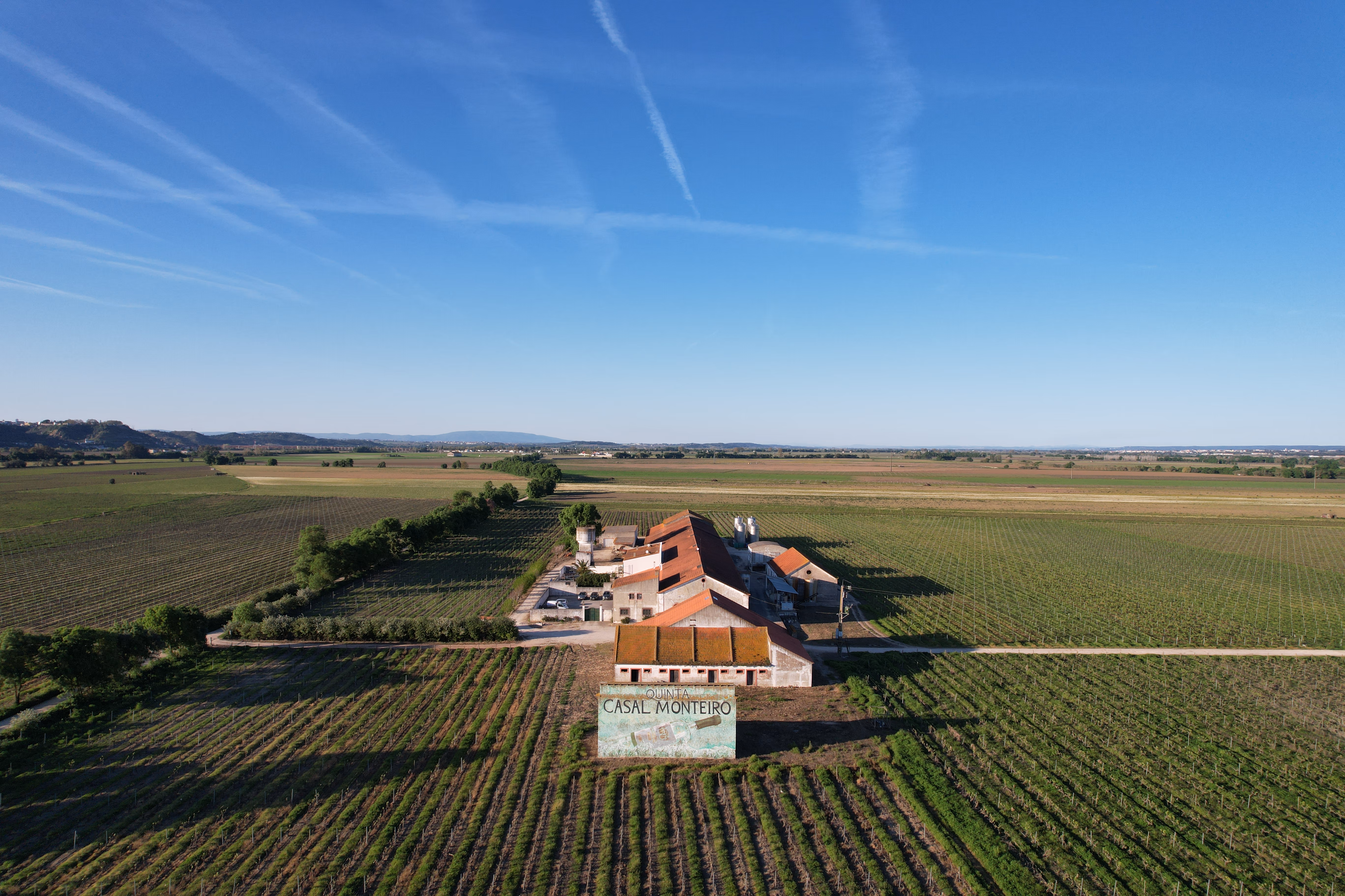 Aerial view of Quinta do Casal Monteiro main building surrounded by vineyard rows under a clear blue sky